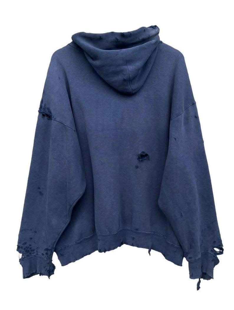 Puede incluir: Una sudadera con capucha azul desgastada con cord&oacute;n de ajuste. La sudadera tiene varios agujeros y bordes deshilachados.
