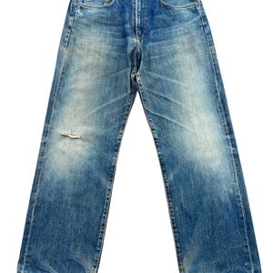May include: Faded blue denim jeans with a distressed look. The jeans have a classic five-pocket design, a button and zipper closure, and a small tear on the left leg. The jeans have a straight leg cut.