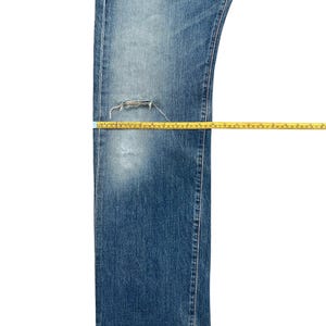 Puede incluir: Vaqueros azules de mezclilla con una zona de rodilla desgastada. Una cinta m&eacute;trica amarilla se coloca sobre los vaqueros para medir la longitud. Los vaqueros tienen un lavado descolorido y un dise&ntilde;o cl&aacute;sico de cinco bolsillos.