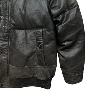 May include: Close-up of a black leather jacket with a quilted design. The jacket features a button-up front, a pocket on the chest, and a ribbed hem. The leather has a worn, distressed appearance.