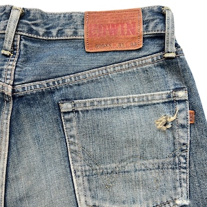 May include: Close-up of blue denim jeans with a distressed pocket. A brown leather patch with the brand name "EDWIN" is visible. The jeans are labeled "505XX 31 33".