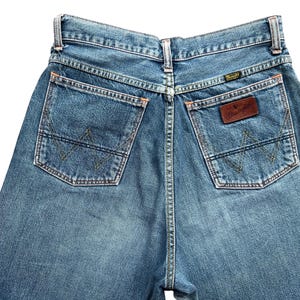May include: Light blue denim jeans with classic five-pocket design. Features include a brown leather patch with the brand name and a signature stitching pattern on the back pockets. The jeans have a straight leg cut.