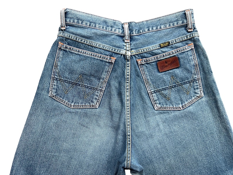 May include: Light blue denim jeans with classic five-pocket design. Features include a brown leather patch with the brand name and a signature stitching pattern on the back pockets. The jeans have a straight leg cut.
