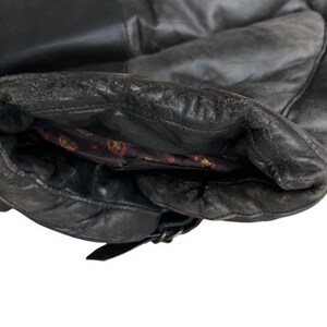 May include: Close-up of a black leather jacket sleeve. The leather shows signs of wear and tear, with a distressed appearance. The interior lining is visible, featuring a patterned design. A buckle detail is present near the cuff.