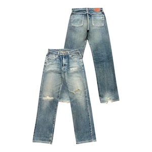 May include: Two pairs of light blue denim jeans with a faded wash and distressed details. One pair is laid flat, the other is standing upright. Both have a classic five-pocket design and a button fly.