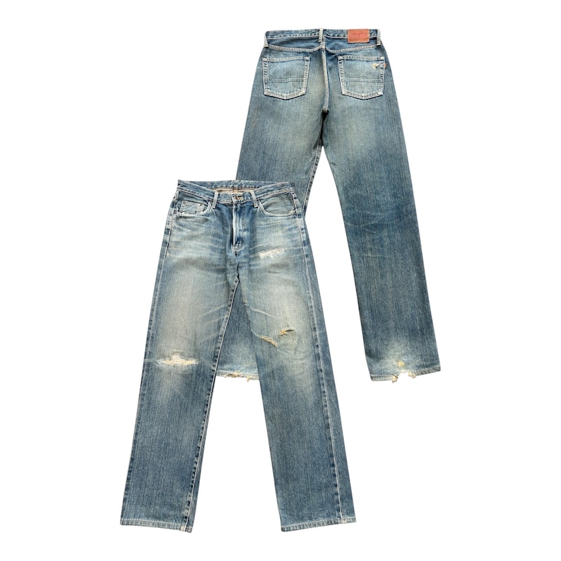 May include: Two pairs of light blue denim jeans with a faded wash and distressed details. One pair is laid flat, the other is standing upright. Both have a classic five-pocket design and a button fly.