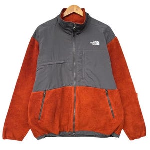 Może przedstawiać: Szara i pomarańczowa kurtka polarowa z zamkiem błyskawicznym i logo "The North Face" na lewej piersi.