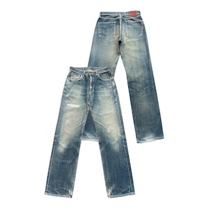 May include: Two pairs of faded blue denim jeans. One pair is laid flat, showing the front, while the other is upright, displaying the back pockets and a leather patch. The jeans have a classic, worn look.