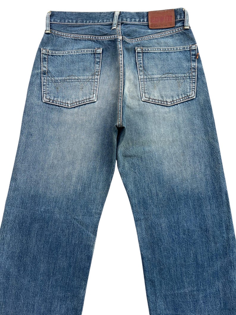 Puede incluir: Vista trasera de unos vaqueros de mezclilla azules con dos bolsillos traseros y un parche de cuero marr&oacute;n. Los vaqueros tienen un lavado descolorido y un dise&ntilde;o cl&aacute;sico de cinco bolsillos. La mezclilla es de peso medio.