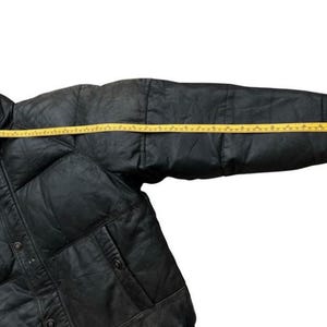 May include: Black puffer jacket with a yellow measuring tape across the sleeve. The jacket has a button closure and two pockets. The sleeve measures approximately 30 inches.
