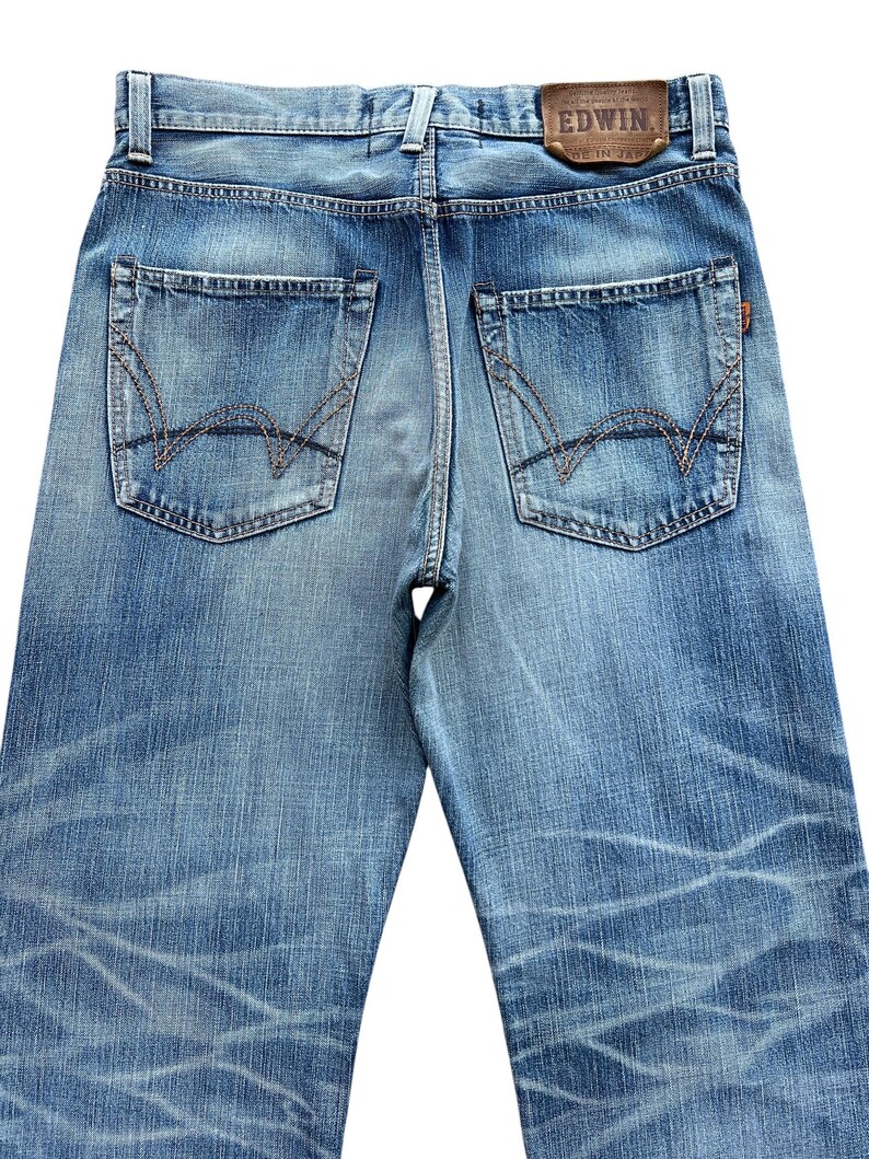 Pu&ograve; includere: Jeans di denim blu chiaro con dettagli usurati e cuciture a vista. Le tasche posteriori presentano un design unico e un'etichetta in pelle marrone con il marchio "EDWIN" &egrave; visibile. Fatto in Giappone.