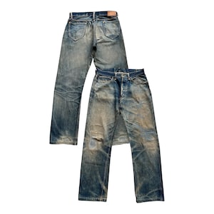 May include: Two pairs of vintage blue denim jeans with a worn, faded appearance. The jeans have a classic five-pocket design, button fly, and a leather patch. The denim has a distressed look with lighter patches and fading throughout.