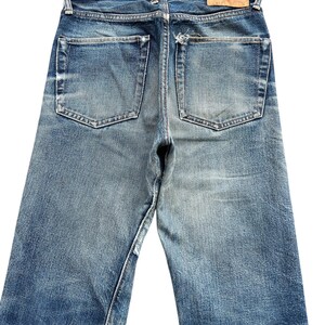 Pu&ograve; includere: Jeans in denim blu sbiadito con un classico design a cinque tasche. I jeans mostrano segni di usura, con un aspetto invecchiato. Una toppa in pelle &egrave; visibile sul girovita posteriore. I jeans hanno un taglio dritto.