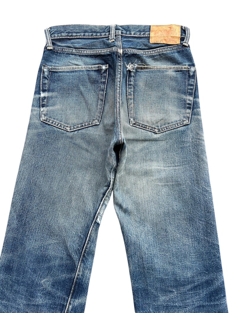 Pu&ograve; includere: Jeans in denim blu sbiadito con un classico design a cinque tasche. I jeans mostrano segni di usura, con un aspetto invecchiato. Una toppa in pelle &egrave; visibile sul girovita posteriore. I jeans hanno un taglio dritto.