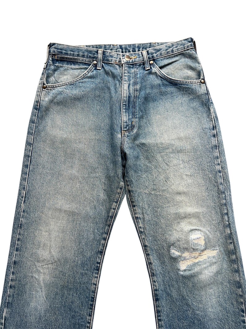 K&ouml;nnte beinhalten: Hellblaue Jeans aus Denim mit verwaschener Optik und Used-Details. Die Jeans haben einen klassischen F&uuml;nf-Taschen-Stil, einen Knopf- und Rei&szlig;verschluss und eine entspannte Passform. Der Denim hat ein abgenutztes Aussehen mit einem Riss am rechten Bein.