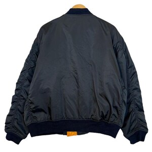 May include: A black bomber jacket with a navy blue collar and cuffs. The jacket has a smooth, shiny texture and a ribbed hem. The jacket is hanging on a wooden hanger.