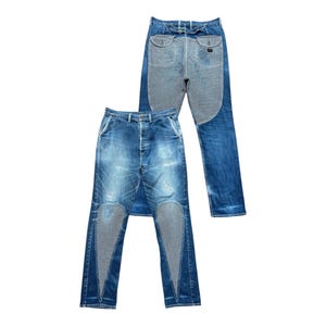 May include: Two pairs of blue denim jeans. One pair is laid flat, showing the front with a button fly and distressed wash. The other pair is folded, revealing the back. Both pairs feature contrasting textured panels.