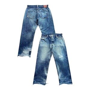 Puede incluir: Un par de pantalones vaqueros de mezclilla azul con acabado desgastado, dobladillos deshilachados y signos visibles de uso. Incluyen cierre de botones, dos bolsillos traseros con costuras, una etiqueta de cuero marrón y un lavado desteñido.