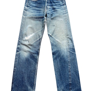 Pu&ograve; includere: Jeans in denim blu sbiadito con chiusura a bottoni e classico design a cinque tasche. I jeans mostrano segni di usura con aree rovinate e un lavaggio chiaro, creando un'estetica vintage. I jeans sono a gamba dritta.