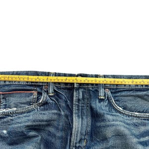 Puede incluir: Primer plano de unos vaqueros azules con una cinta m&eacute;trica amarilla sobre la cintura. Los vaqueros tienen un dise&ntilde;o cl&aacute;sico de cinco bolsillos, con desgaste visible. La cinta m&eacute;trica muestra la medida de la cintura en cent&iacute;metros.