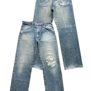 K&ouml;nnte beinhalten: Zwei Paar Vintage-Jeans aus blauem Denim. Ein Paar liegt &uuml;ber dem anderen. Die Jeans haben ein klassisches F&uuml;nf-Taschen-Design, eine verblasste Waschung und einen abgenutzten Bereich an der Vorderseite eines Beins. Die Ges&auml;&szlig;taschen weisen ein markantes Nahtmuster auf.
