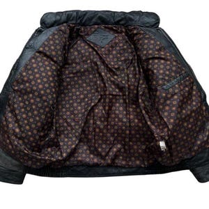 May include: Black leather jacket with a quilted collar and a patterned interior lining. The jacket has a classic design with a front zipper and pockets. The interior lining features a repeating pattern of small circles in shades of brown and gold.