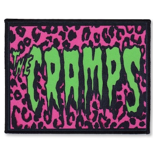 Peut inclure: Un patch brodé noir et vert avec un fond imprimé léopard rose. Le patch présente le texte "THE CRAMPS" dans une police d'écriture qui coule.
