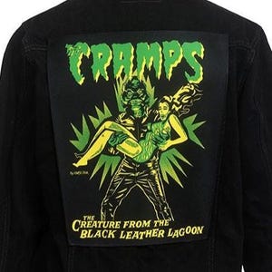 May include: Black denim jacket with a green and black patch on the back. The patch features the text "The Cramps" and an illustration of a creature from the black lagoon carrying a woman.