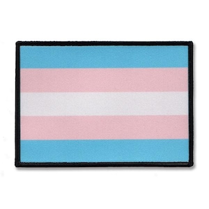 Może przedstawiać: Prostokątna naszywka z flagą dumy osób transpłciowych. Flaga ma poziome paski w kolorze jasnoniebieskim, różowym i białym, z czarną obwódką. Naszywka jest prawdopodobnie wykonana z tkaniny i przeznaczona do przyszywania lub naprasowywania na odzież lub akcesoria.