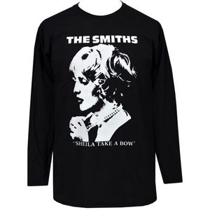 May include: Black long-sleeve shirt featuring a white graphic of a woman's profile, a pearl necklace, and the text "THE SMITHS" above the image. Below the image is the text "SHEILA TAKE A BOW".