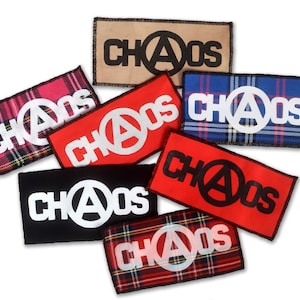 Op de afbeelding: Een verzameling van zeven strijkbare patches met het woord "CHAOS" en een anarchiesymbool in verschillende kleuren en patronen, waaronder rood, zwart, blauw en beige.