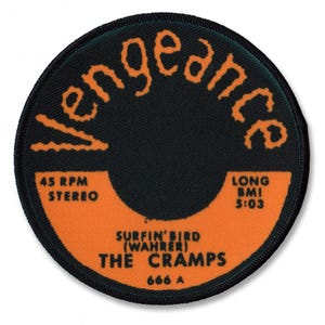 Può includere: Un cerotto rotondo nero e arancione con il testo "Vengeance" in un font stilizzato attorno al bordo. Il centro del cerotto presenta un disco in vinile nero con il testo "45 RPM Stereo", "Long BMI 5:03", "Surfin' Bird (Wahrer)", "The Cramps" e "666 A".
