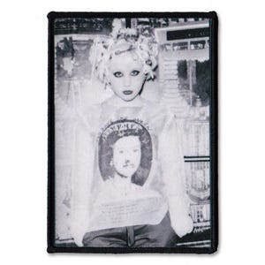 May include: A rectangular black and white fabric patch featuring a photographic print of a person with curly hair wearing a shirt with a portrait of Queen Elizabeth II. The patch has a thick black embroidered border and a high-contrast aesthetic.