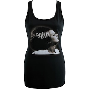 Peut inclure: Débardeur noir avec une image en noir et blanc d'une femme de profil avec une coiffure élaborée. L'image est centrée sur le devant du débardeur. Le débardeur a un col rond et un design sans manches.