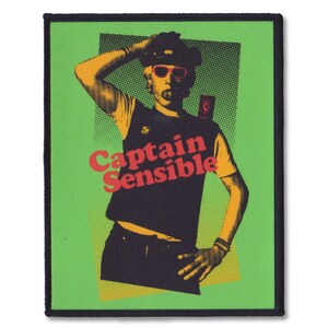 May include: A rectangular patch with a pop art style illustration of a person in sunglasses, a cap, and a vest. The text "Captain Sensible" is in red and orange. The background is green with a black border.