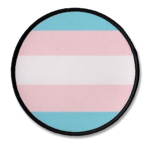 Pode incluir: Um patch redondo com a bandeira do orgulho transgênero. O design inclui listras horizontais em azul claro, rosa e branco, com uma borda preta. O patch é um símbolo da comunidade transgênero.
