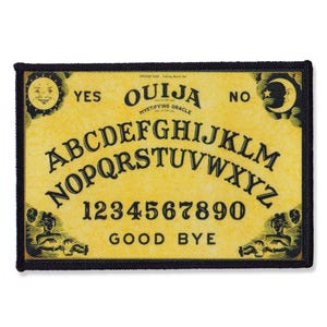 May include: A yellow and black Ouija board patch with the letters A-Z, numbers 1-9, 0, and the words "YES", "NO", "GOOD BYE", and "OUIJA MYSTIFYING ORACLE".