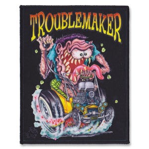 Puede incluir: Un parche negro con una ilustración de dibujos animados de un monstruo conduciendo un hot rod. El monstruo tiene una boca grande con una lengua rosa que sobresale. El texto "Troublemaker" está escrito en letras amarillas y naranjas sobre el monstruo.