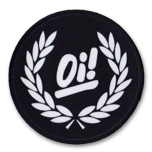 Peut inclure: Écusson rond noir avec le mot "Oi!" en blanc, entouré d'une couronne de laurier blanche. Le texte est stylisé. Le patch a une bordure noire et est de forme circulaire.