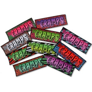 Può includere: Una collezione di toppe rettangolari con il nome della band "The Cramps" in un font in stile graffiti. Le toppe hanno vari sfondi con stampa animalier, tra cui leopardo, zebra e ghepardo, con vivaci combinazioni di colori come rosa, verde e viola.