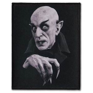 May include: A monochrome patch depicting a bald man with a pale complexion, sharp features, pointed ears, and long fingernails. He wears a dark cloak. The patch has a black border and is a classic horror image.