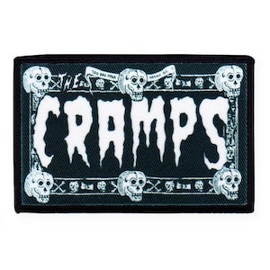 May include: Black and white embroidered patch with the text "The Cramps" and a skull design. The patch has a black border and a green background.