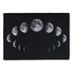 May include: A rectangular black patch featuring a detailed graphic of the lunar cycle. The design displays various phases of the moon, ranging from thin crescents to a full moon, arranged in a curved, elliptical formation against a solid black background.