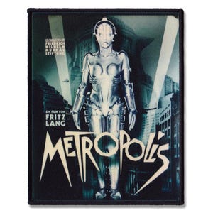 Puede incluir: Un parche en blanco y negro con un diseño de cartel de película vintage. El cartel presenta a una mujer robot en una ciudad futurista con el texto "Metropolis" en una fuente audaz y estilizada.