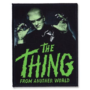 Peut inclure: Un écusson brodé noir et vert représentant une créature à la peau verte et aux griffes acérées. Le texte "The Thing from Another World" est écrit en vert sous la créature.