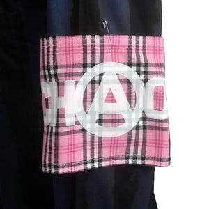Può includere: Una toppa in tessuto a quadri rosa e bianco con la scritta "CHAOS" a lettere bianche e un simbolo di anarchia bianco. La toppa è appuntata su un tessuto blu scuro.