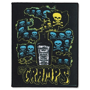 Puede incluir: Parche negro con un diseño gráfico de calaveras, huesos cruzados y una botella. El diseño incluye el texto "THE CRAMPS" en una fuente amarilla estilizada. La botella tiene un texto difícil de leer.