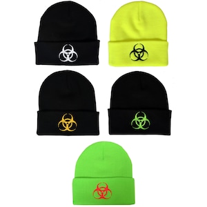 Puede incluir: Cinco gorros de punto con un símbolo de riesgo biológico en diferentes colores. Los gorros son negros, amarillo neón, verde neón y negros con un símbolo de riesgo biológico amarillo y verde.