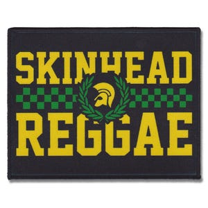 以下が含まれることがあります： 黒地に黄色の文字で「SKINHEAD REGGAE」と書かれたパッチ。文字の下には緑と白の市松模様。文字と市松模様の間に、金色のヘルメットが入った緑の月桂樹の輪が中央に配置されている。
