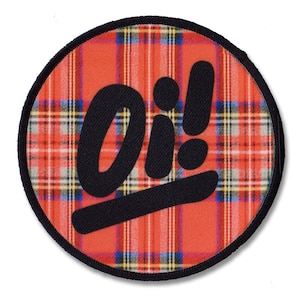 Könnte beinhalten: Ein runder, rot-schwarzer Patch mit einem schwarzen "Oi!" in einer stilisierten Schriftart auf einem rot-schwarzen Karomuster.